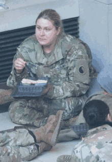 a female soldier named robbins sits on the floor eating food