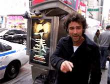 a man standing in front of a phone booth with a poster on it that says ' dirty shades of grey '