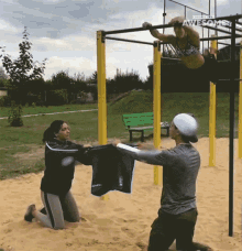 a woman is doing a pull up on a bar while a man holds a black shirt over her head