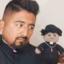 a man with a beard is holding a crocheted priest doll .