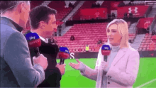 a woman is talking into a microphone on a soccer field with two men .