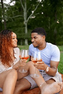 a man and a woman are sitting on the ground holding wine glasses