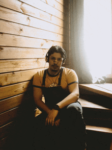 a man wearing headphones and a shirt that says joker sits in front of a wooden wall