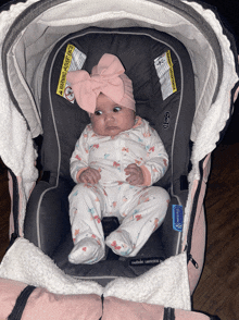 a baby wearing a pink bow is sitting in a car seat with a warning sticker on it