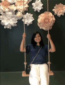 a woman sits on a swing in front of a wall of paper flowers