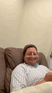 a man wearing a hospital gown is smiling while laying on a couch