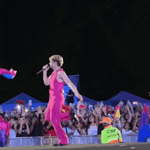 a woman in a pink jumpsuit stands on a stage in front of a crowd and a sign that says csr