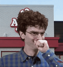 a man wearing glasses and a mustache is covering his mouth in front of a brick building with the letter a on it