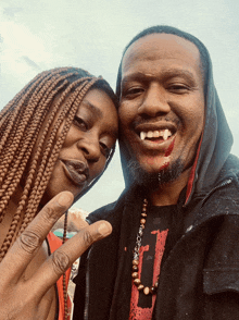 a man with vampire teeth and a woman with braids posing for a photo