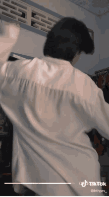 a man in a white shirt is dancing in a room with clothes hanging on the wall behind him