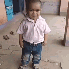 a little boy wearing a white shirt and blue jeans is standing on a sidewalk with his hands in his pockets .