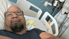 a man with a beard and glasses is laying in a hospital bed