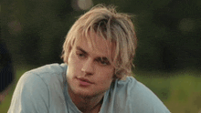 a young man with blonde hair is wearing a light blue shirt and looking at the camera .