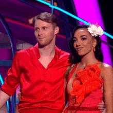 a man in a red shirt is standing next to a woman in a red dress with flowers in her hair