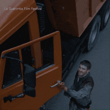 a man is standing next to an orange truck with the words la guarimba film festival written on the bottom