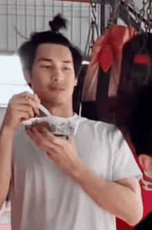 a man in a white shirt is eating noodles with chopsticks from a bowl .