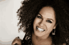 a woman with curly hair is smiling for the camera and wearing earrings .