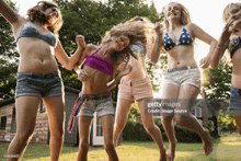 a group of young girls in bikinis and shorts are dancing in a circle