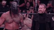 two men are standing next to each other in a wrestling ring and one of them is wearing a mask .