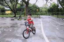 a young boy is riding a bike on a wet street with a sign that says ' a ' on it