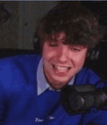 a young man in a blue sweater is sitting in front of a microphone and smiling .