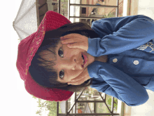 a little girl wearing a red hat and a blue shirt is making a face