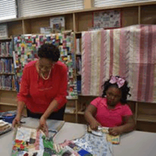 a woman and a girl are sitting at a table making a quilt .