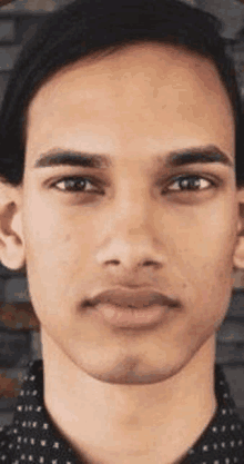 a close up of a young man 's face wearing a black polka dot shirt .