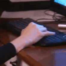 a person 's hand is typing on a keyboard with a monitor in the background