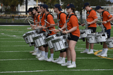 a group of people playing drums with one wearing an orange shirt that says ' uc ' on it