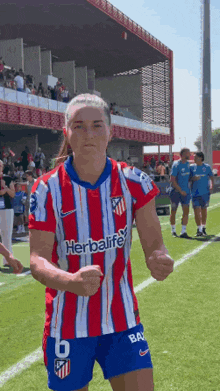 a woman is standing on a soccer field wearing a red and white striped shirt with the word herbalife on it .