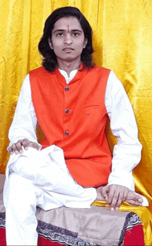 a young man wearing an orange vest and white pants sits on a stool