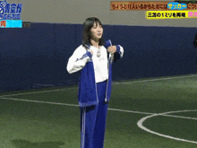 a woman in a blue tracksuit is standing on a soccer field in front of a sign that says soccer