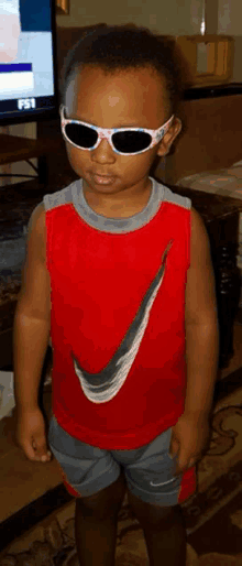 a young boy wearing sunglasses and a red shirt is standing in front of a television .