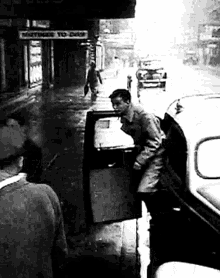 a black and white photo of a man getting out of a car under a sign that says nothing to do