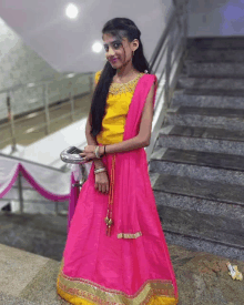 a girl in a yellow top and pink skirt is standing on stairs