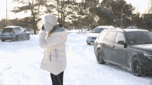 a woman in a white coat is standing in the snow near a car with a license plate that says lkd 88