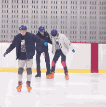 three people are ice skating on a rink and one of them is wearing a t-shirt with a mountain on it