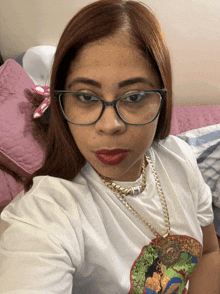 a woman wearing glasses and a necklace is taking a selfie on a bed