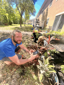 a man in a blue shirt is kneeling down in a garden with potted plants