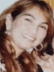 a close up of a woman 's face with a blurry background . she is smiling and wearing hoop earrings .