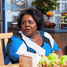 a woman sits at a table with a bowl of green apples in front of a sign that says house of payne