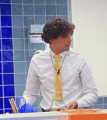 a man wearing a white shirt and a yellow tie stands in front of a blue tiled wall