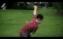 a man in a red striped shirt is throwing a frisbee in a field with the number 4 in the background