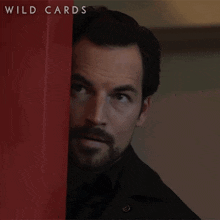 a man peeking out from behind a red wall with wild cards written on the bottom right