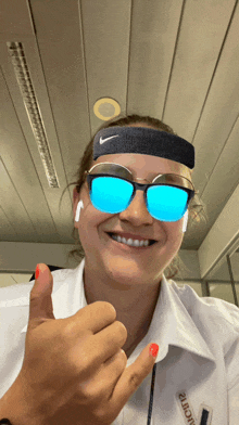 a woman wearing sunglasses and a nike headband giving a thumbs up sign