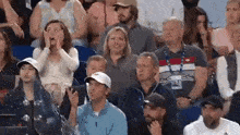 a group of people are sitting in a stadium watching a tennis match and a woman is covering her face with her hands .