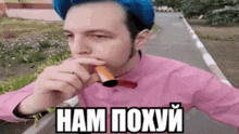 a man wearing a pink shirt and a blue hat is holding a cigarette in his mouth .