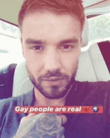 a man with a beard is sitting in a car with the words gay people are real on the bottom