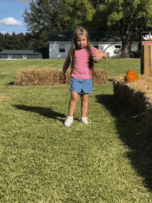 a little girl in a pink shirt and denim shorts stands in a grassy field